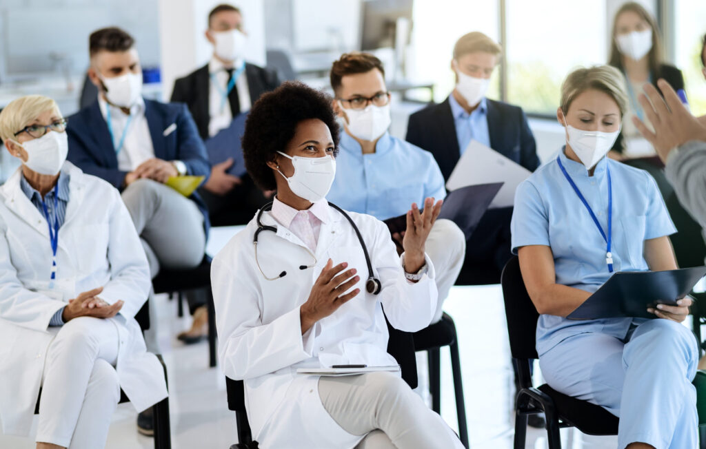 Happy black healthcare worker wearing protective face mask communicating with a businessman who is holding educational event at convention center.