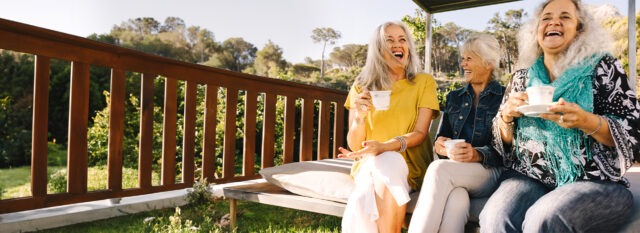 Three women sitting in a backyard laughing while drinking tea