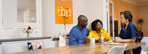 Sciensus nurse chatting with a patient and her partner over tea at their kitchen table