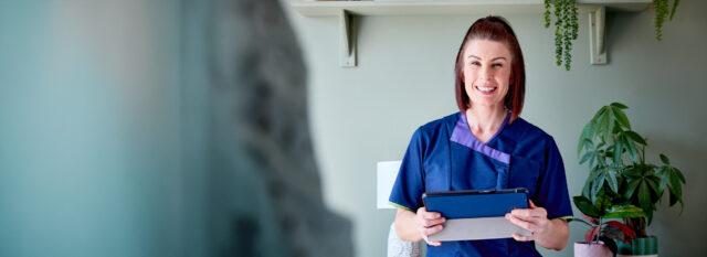 Sciensus nurse holding a tablet and smiling at a patient’s home