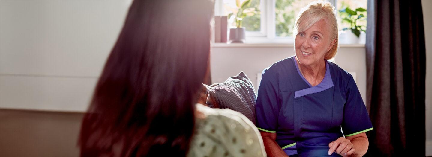 Sciensus nurse sitting on a sofa talking with a patient in her living room